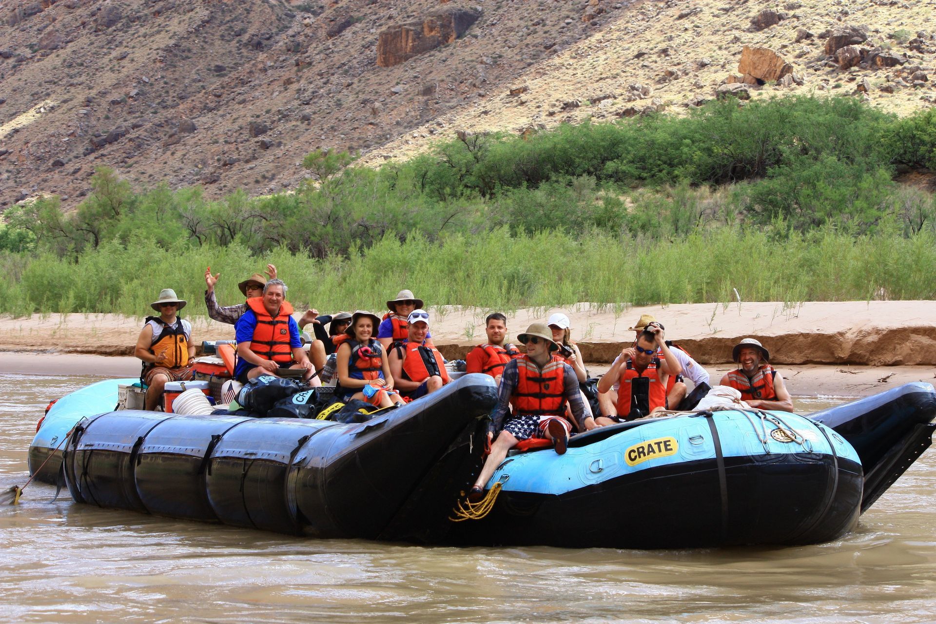 People on a raft floating on a river, with canyon walls in the background.
