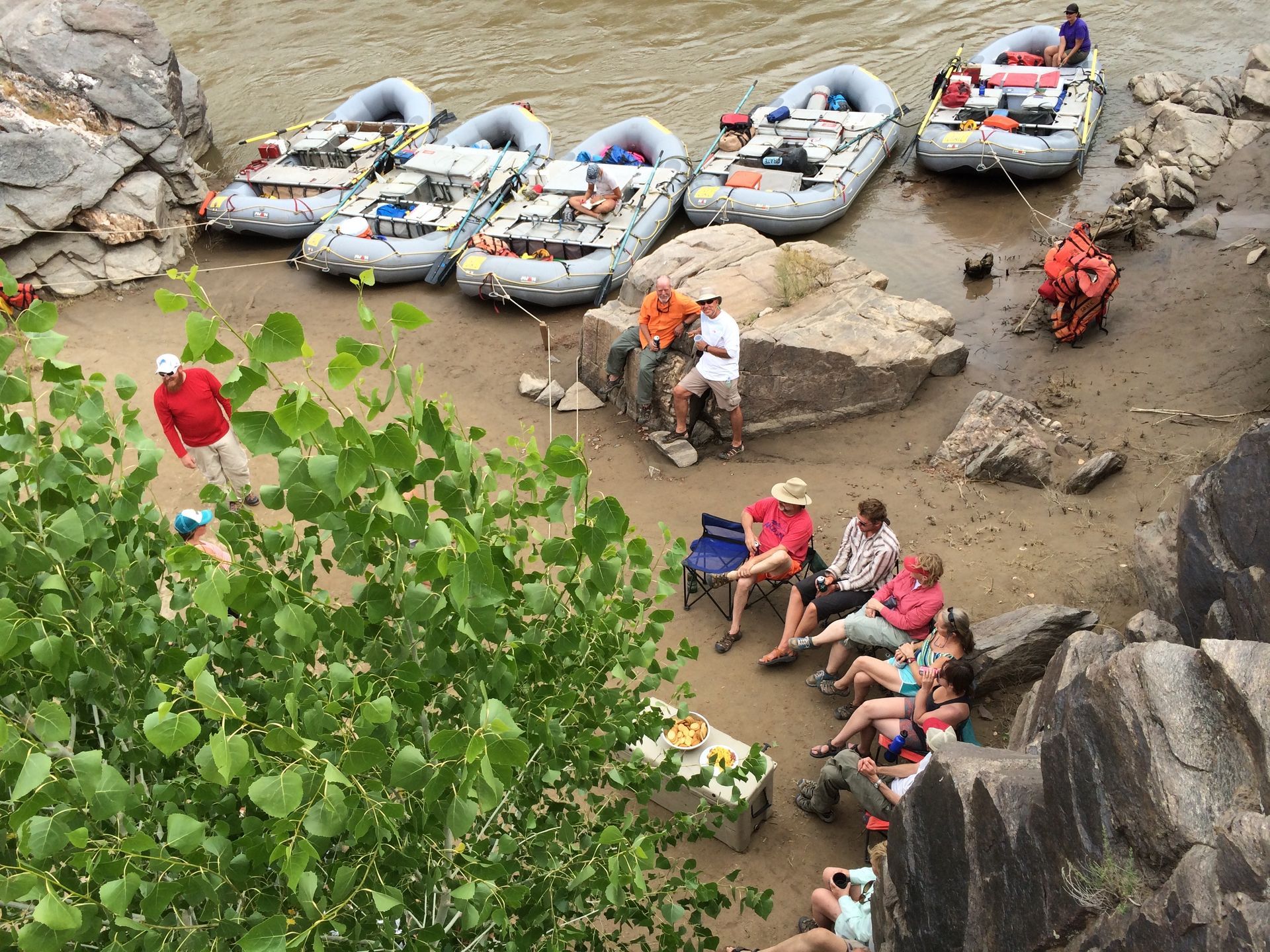 Rafting group at riverside stop: rafts, people resting and chatting near a river. Overlook shot.