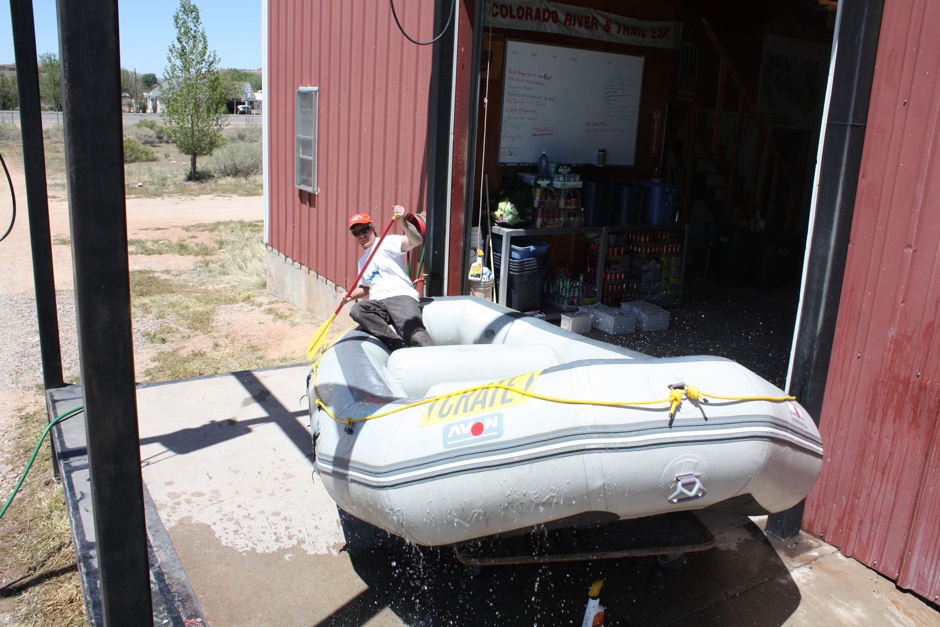 Person washing a raft outside a red building on a sunny day.