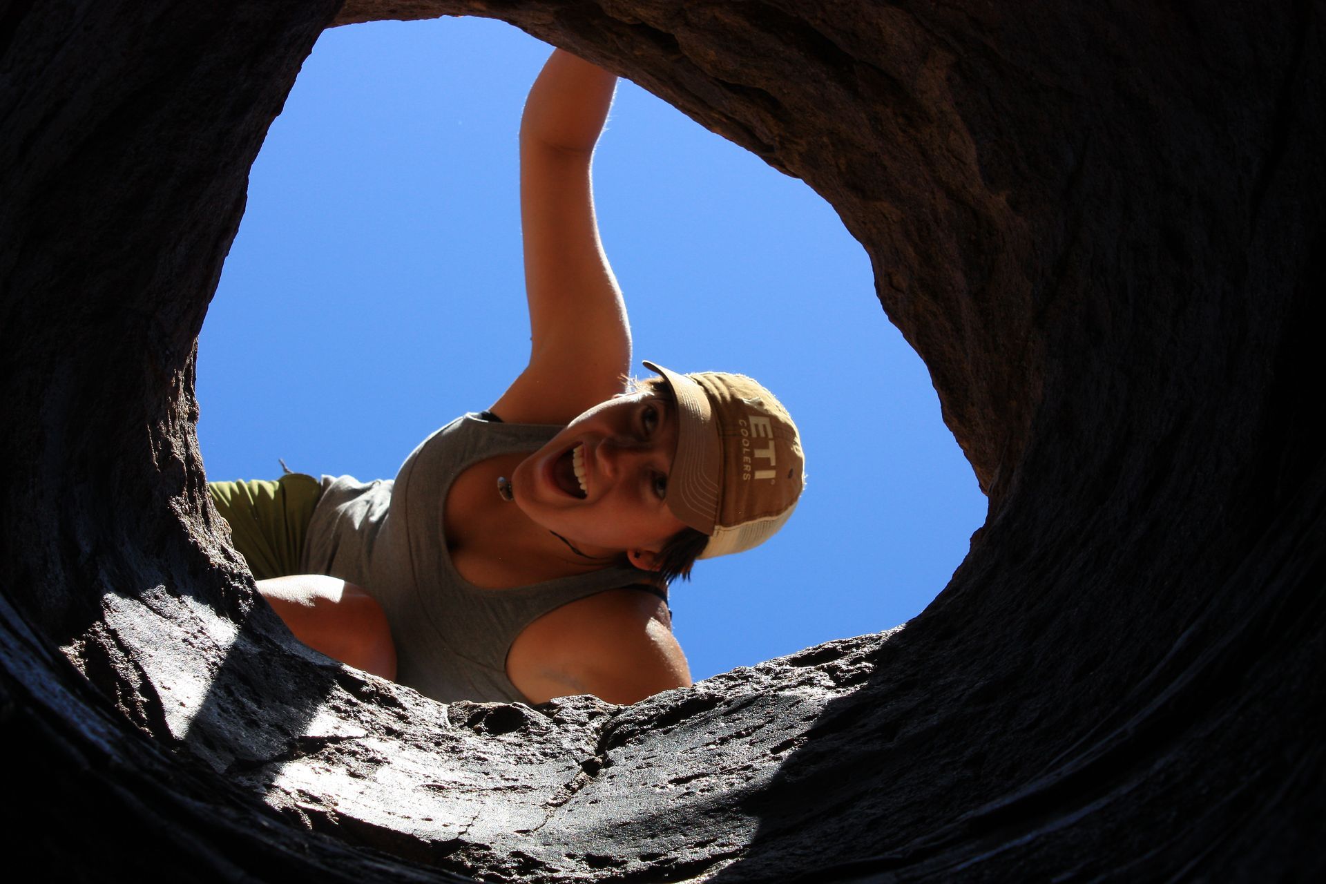 Person looking into a tree trunk hole with a happy expression and blue sky background.