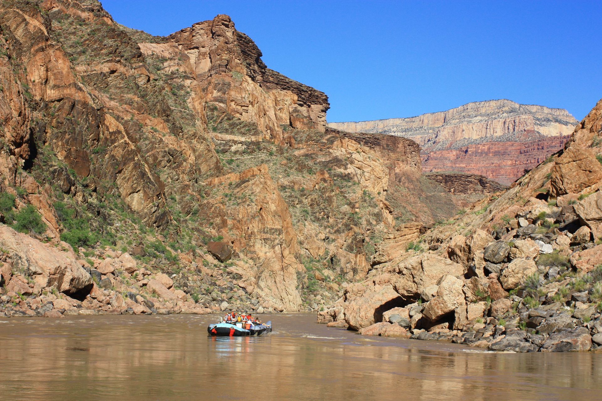 Raft on a muddy river in a canyon. Brown rocks and blue sky.