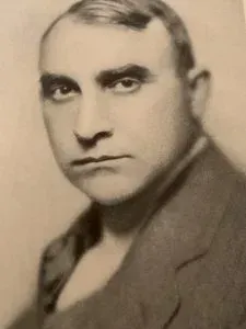 A man in a suit, with dark hair and a serious expression.