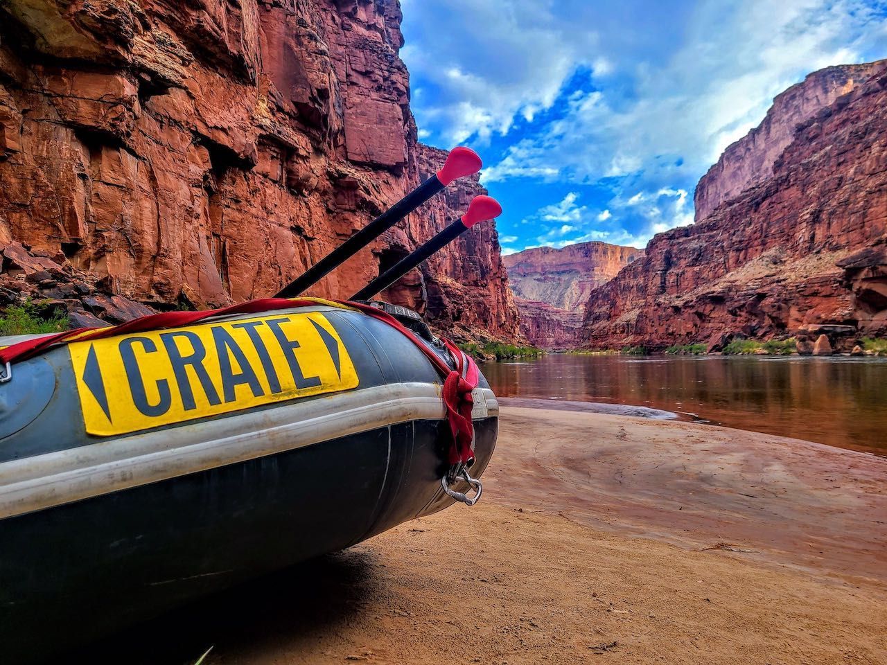 Raft on a sandy riverbank with red rock canyon walls and blue sky.