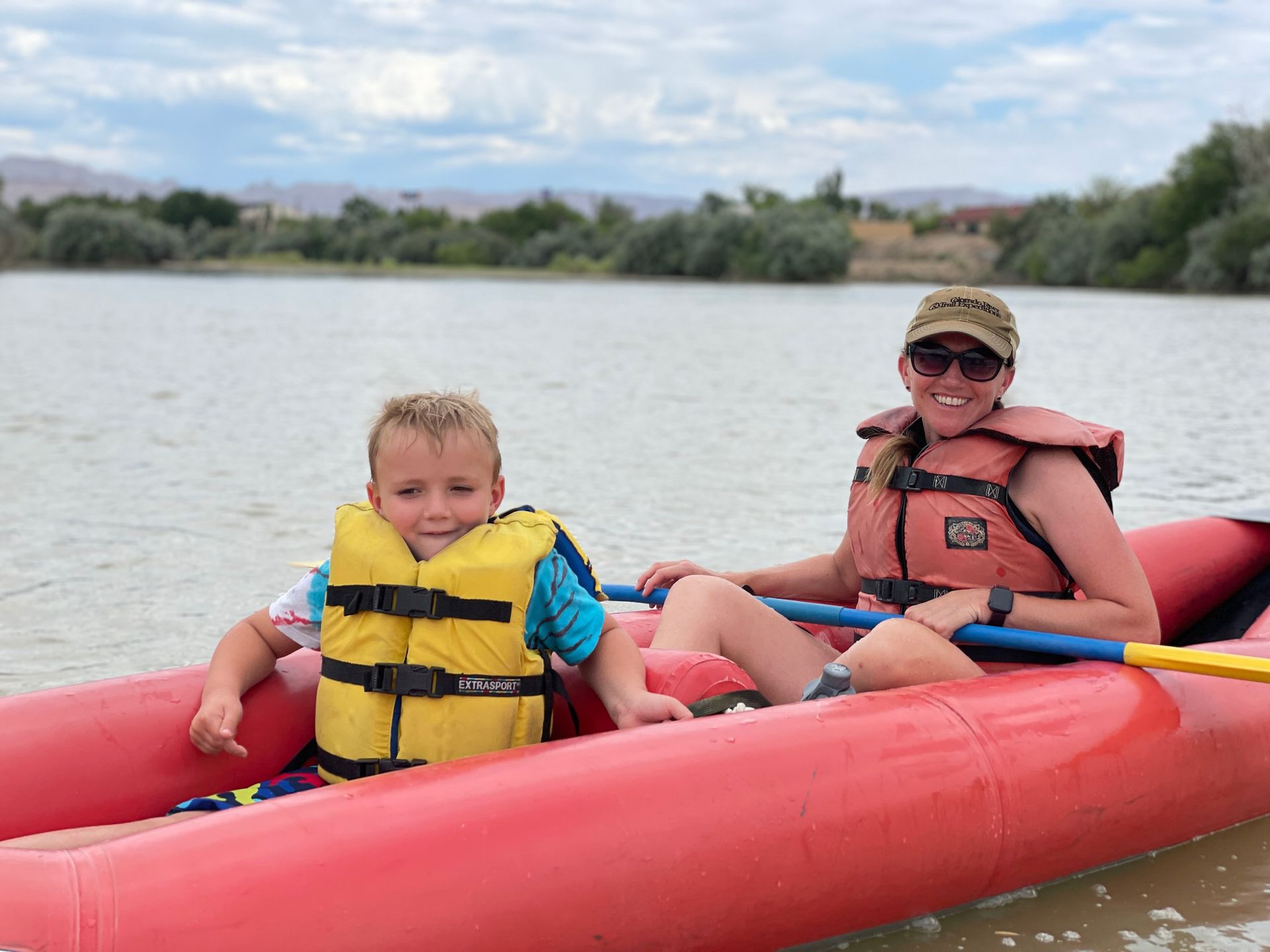 A woman and child in a red kayak on a lake, both wearing life vests.
