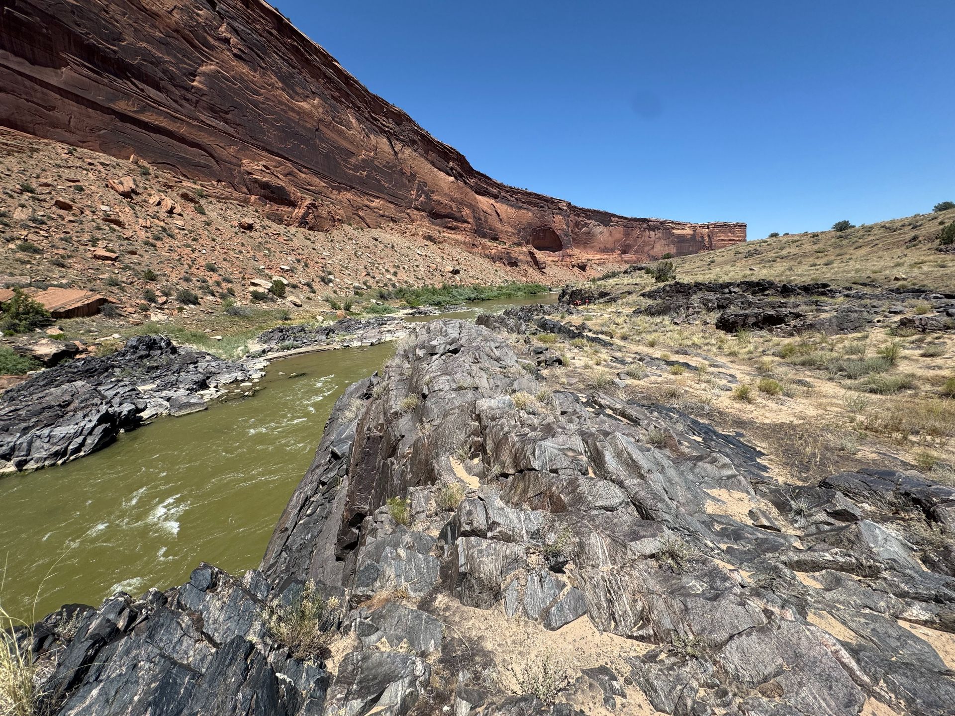 Green river flowing through a rocky canyon under a blue sky.