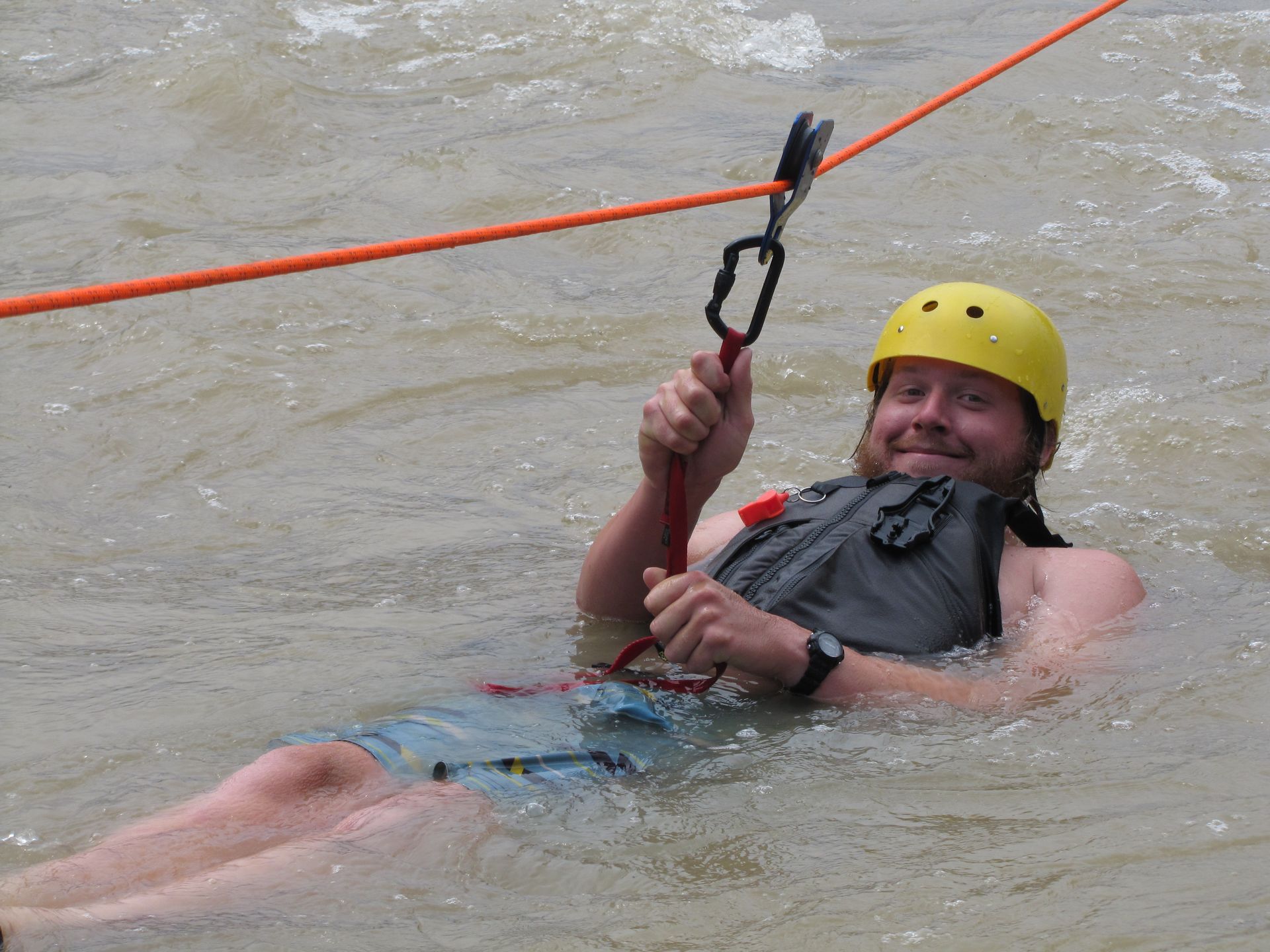 Man in water holding rescue line, wearing helmet and life vest.