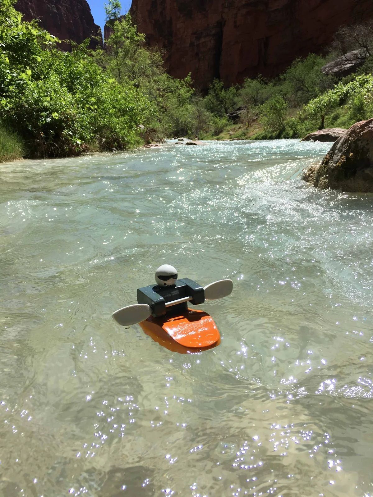 Lego kayaker paddles on clear water in a canyon.