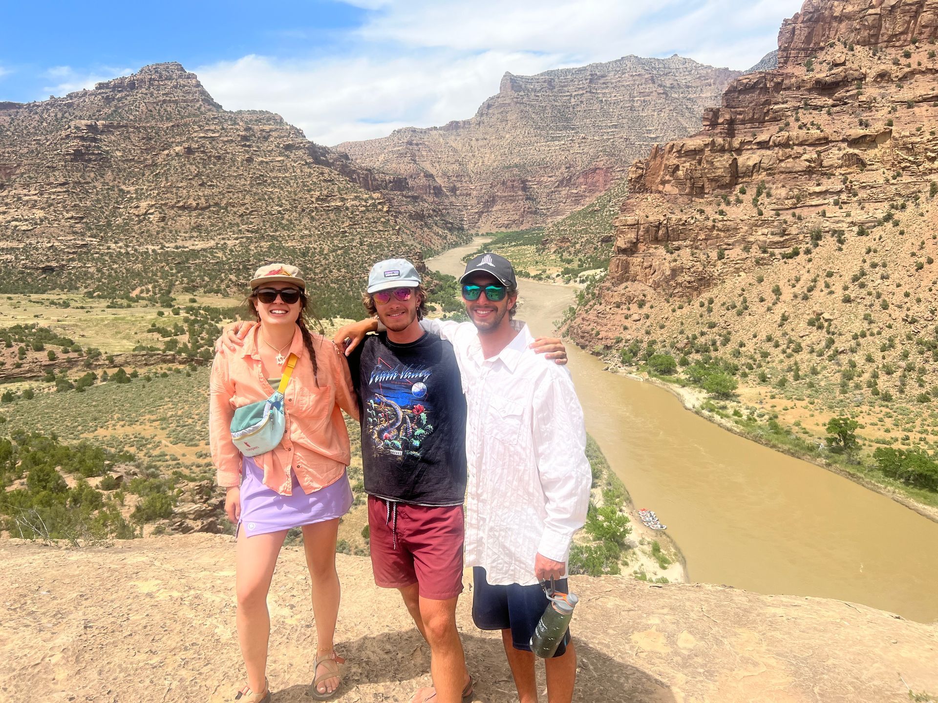 Three people standing on a rocky hillside overlooking a river winding through a canyon.