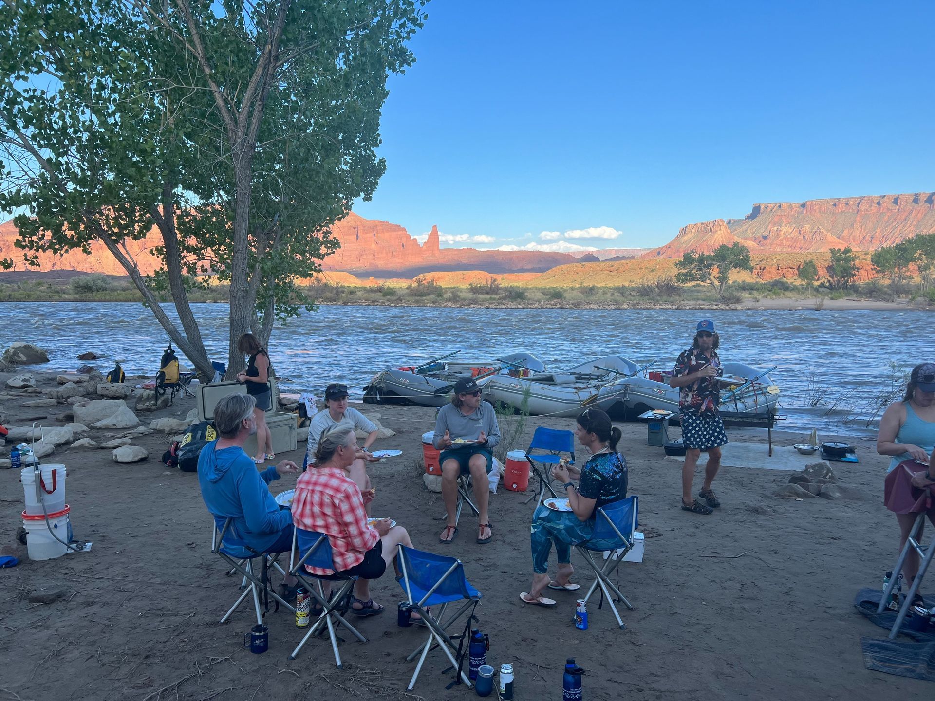 People camping by a river, red rock canyon in background.