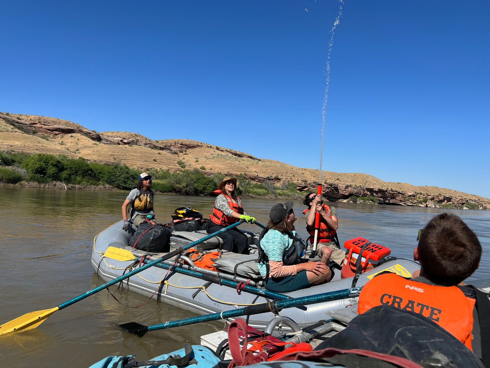 People rafting on a river, under a blue sky, water splashing.