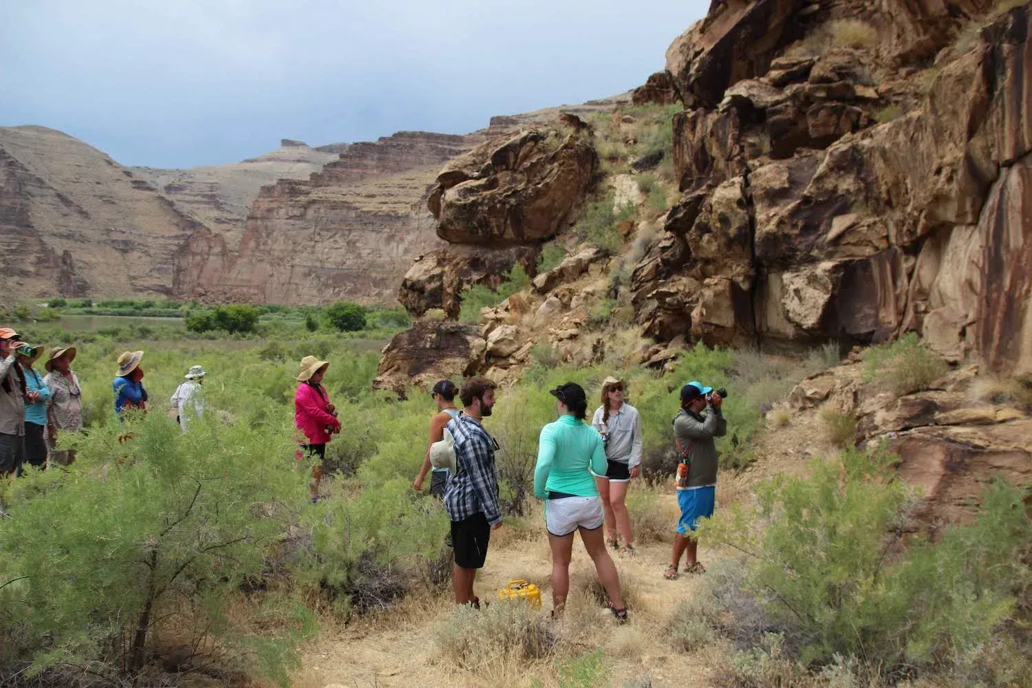 Group of people standing near a rocky cliffside, observing the landscape on a sunny day.