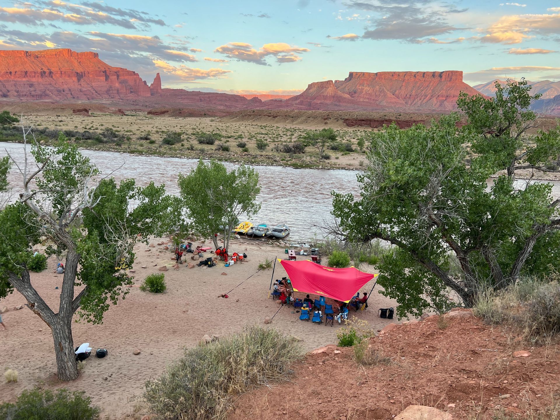 Camp with red canopy near river and canyon in Utah at dusk.