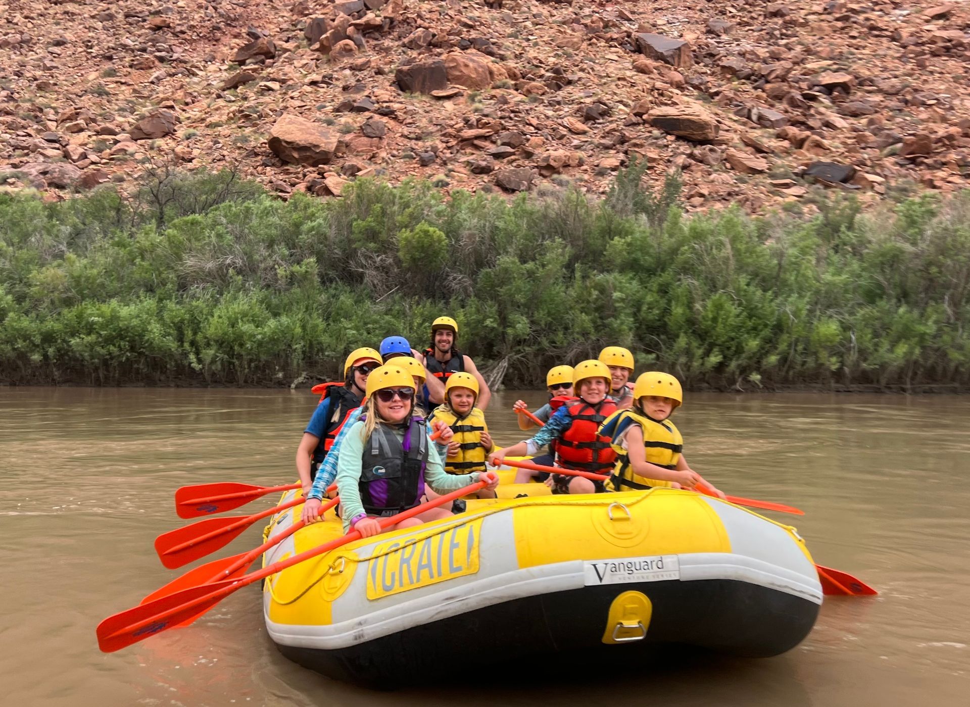People in yellow helmets and life vests on a yellow raft, paddling on a river.