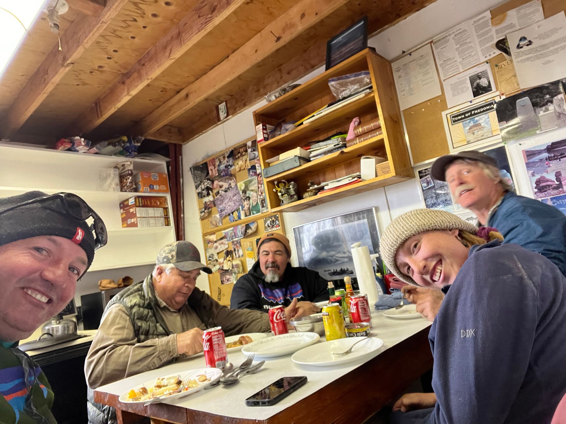 People seated at a table eating, inside a room with cluttered walls.