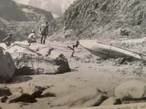 People near a boat on a rocky shore in a canyon.