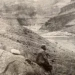 Man seated, looking towards a canyon and river. Black and white photo.