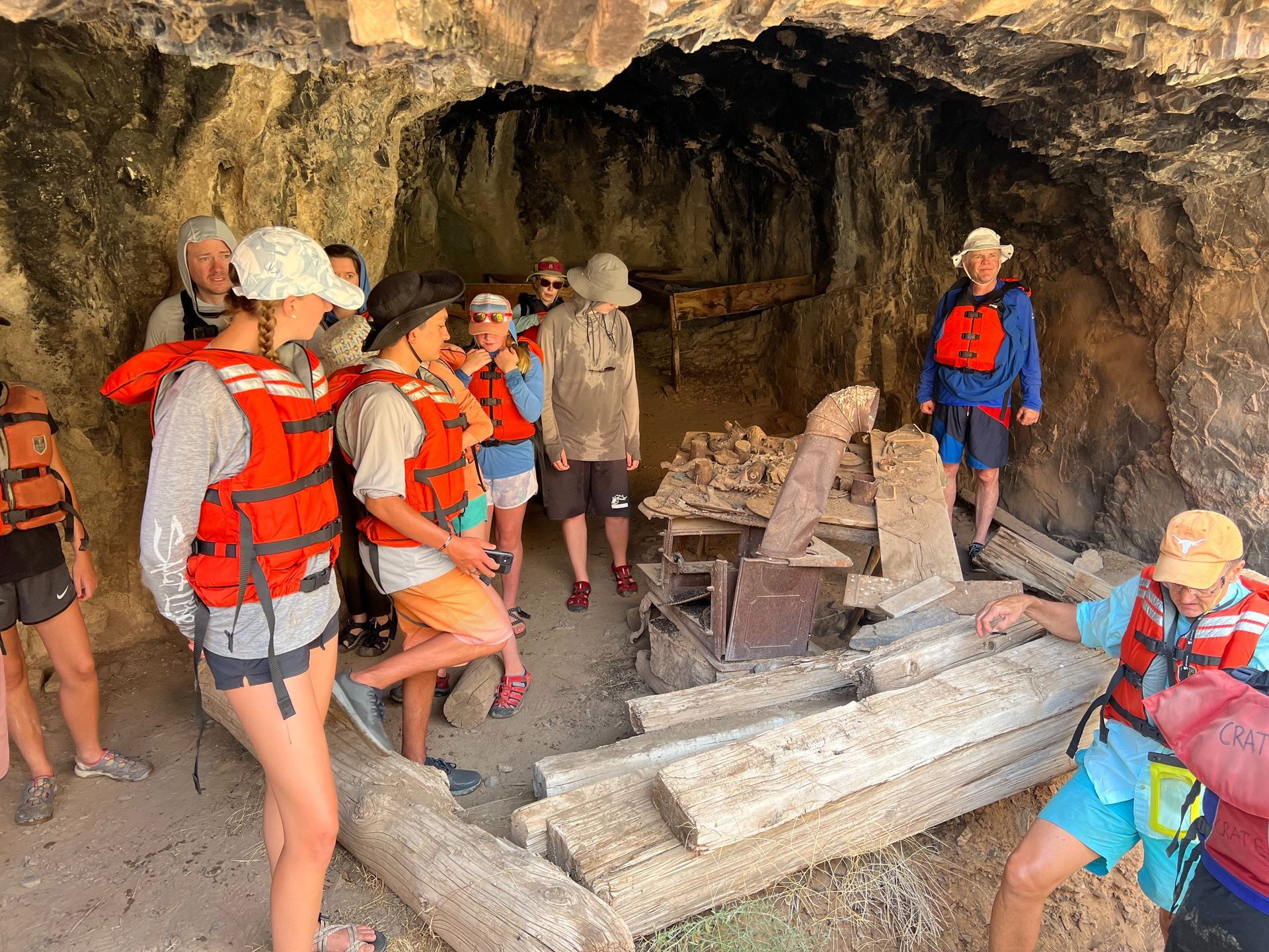 Group in life vests inside a cave, examining old wooden structures.