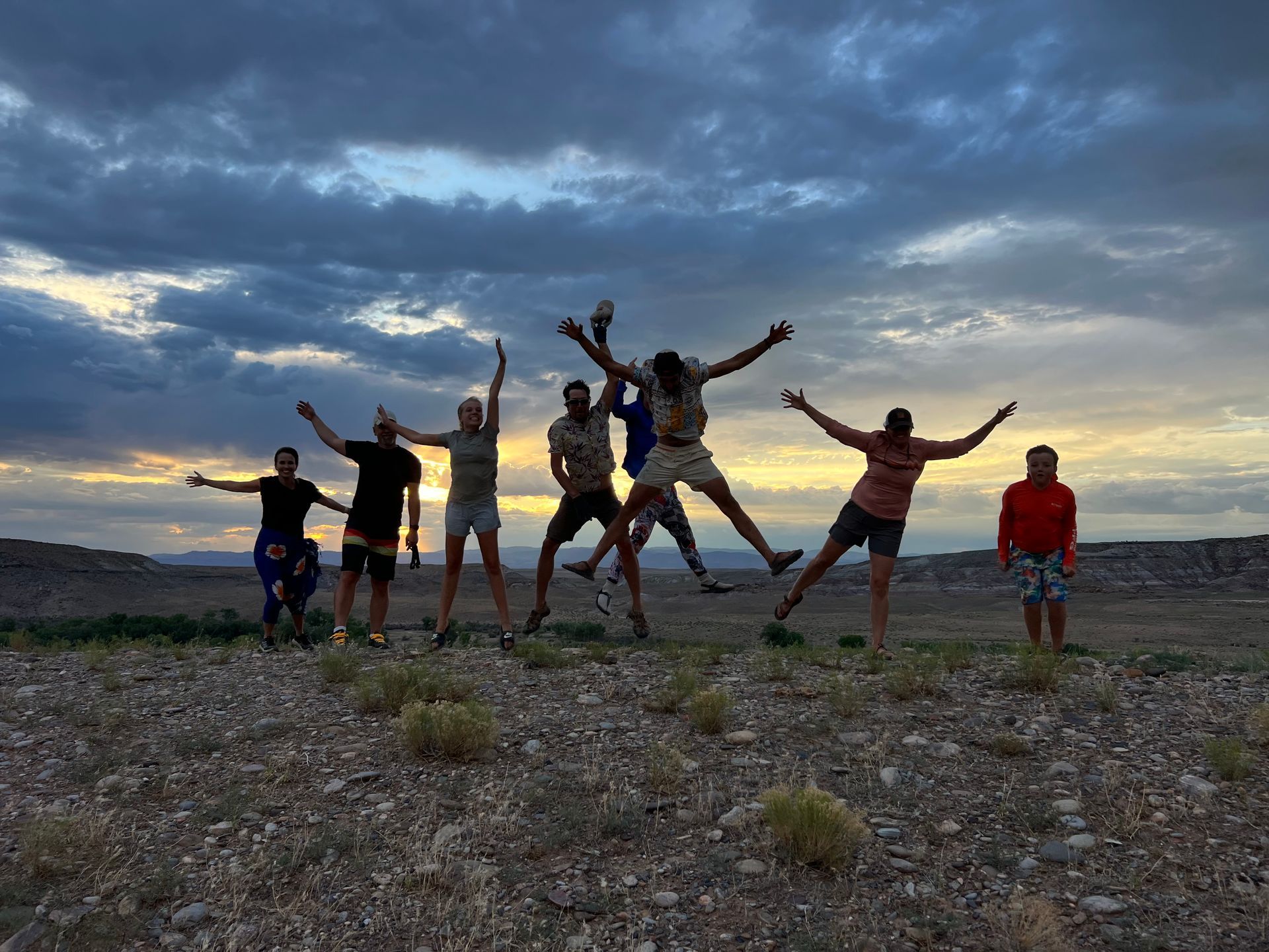 Group of people jumping in silhouette against a sunset in a desert landscape.