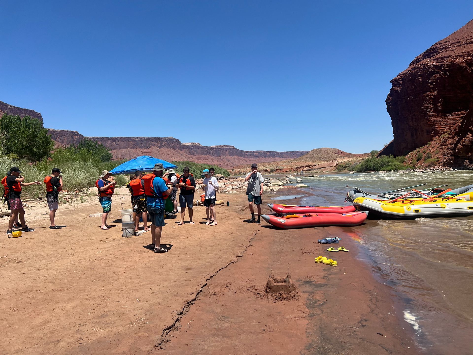 People preparing to raft on a river, with rafts and red rock cliffs in background.