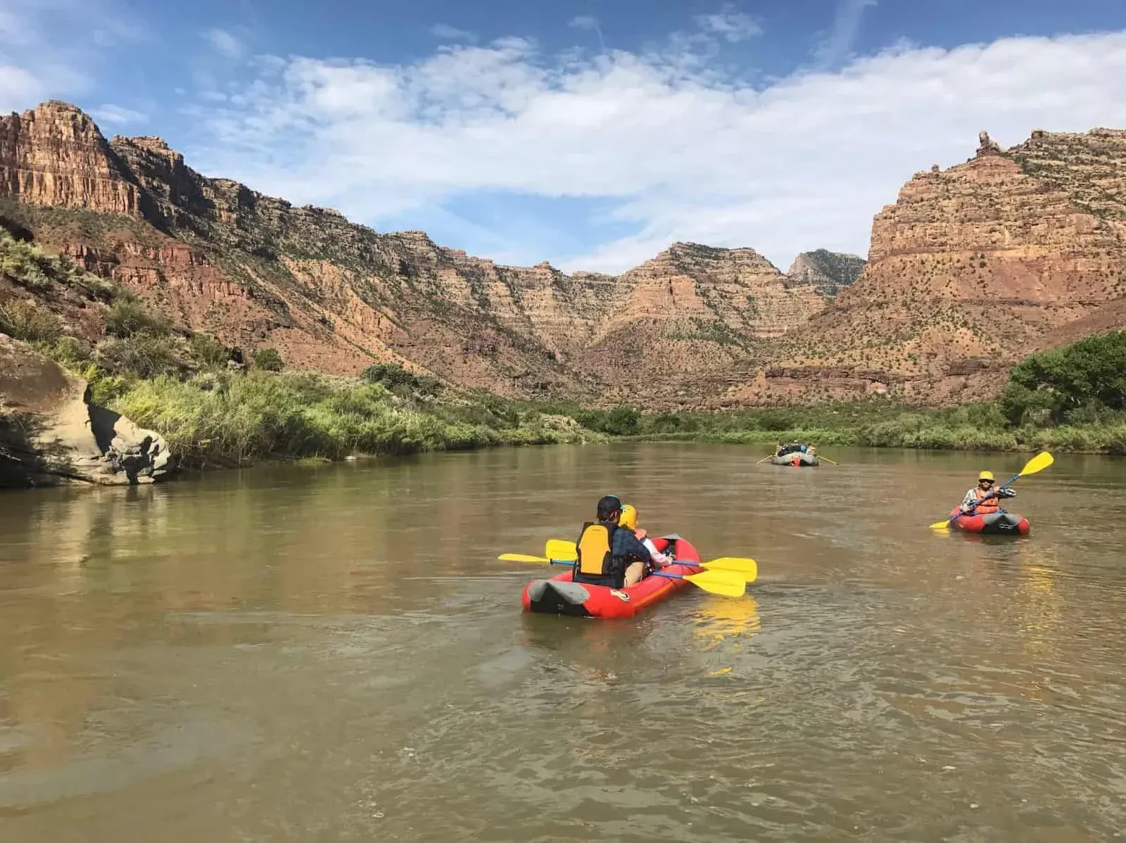Two people on a raft in a canyon river, wearing life vests and hats.