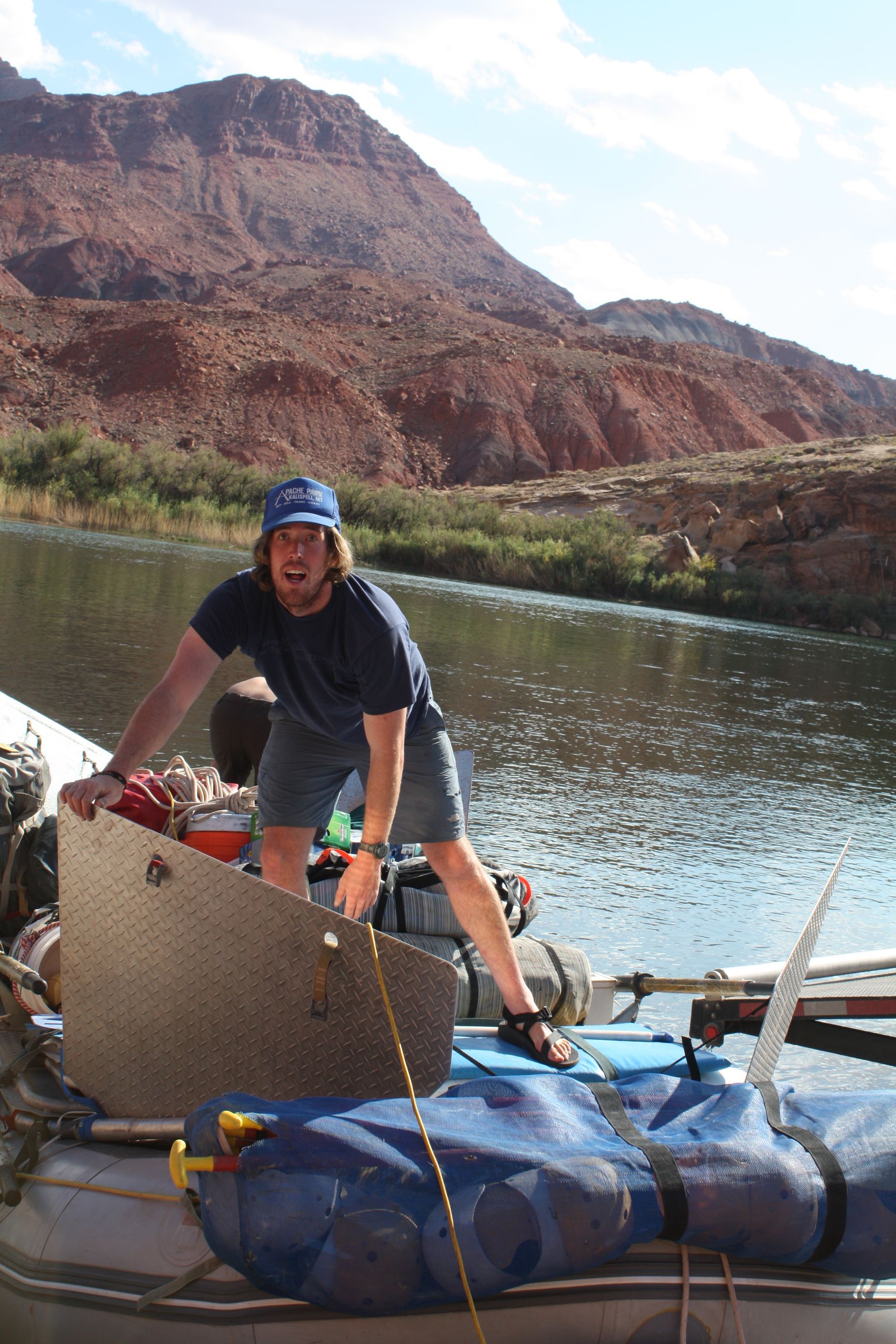 Man on a raft, pulling on a rope near a canyon river. Red rock in the background.