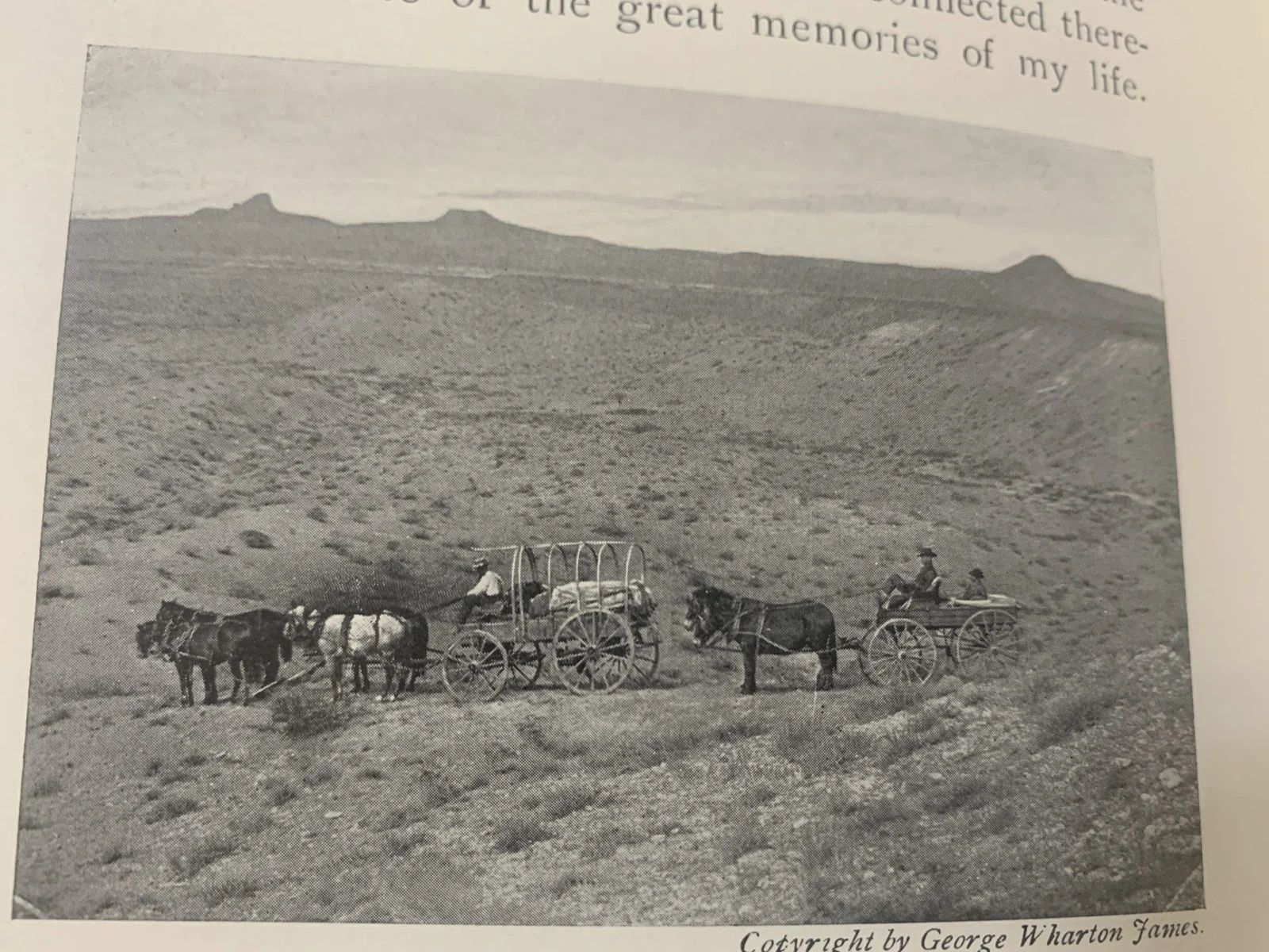An old black and white photo of horse-drawn carriages on a grassy plain with mountains in the background.