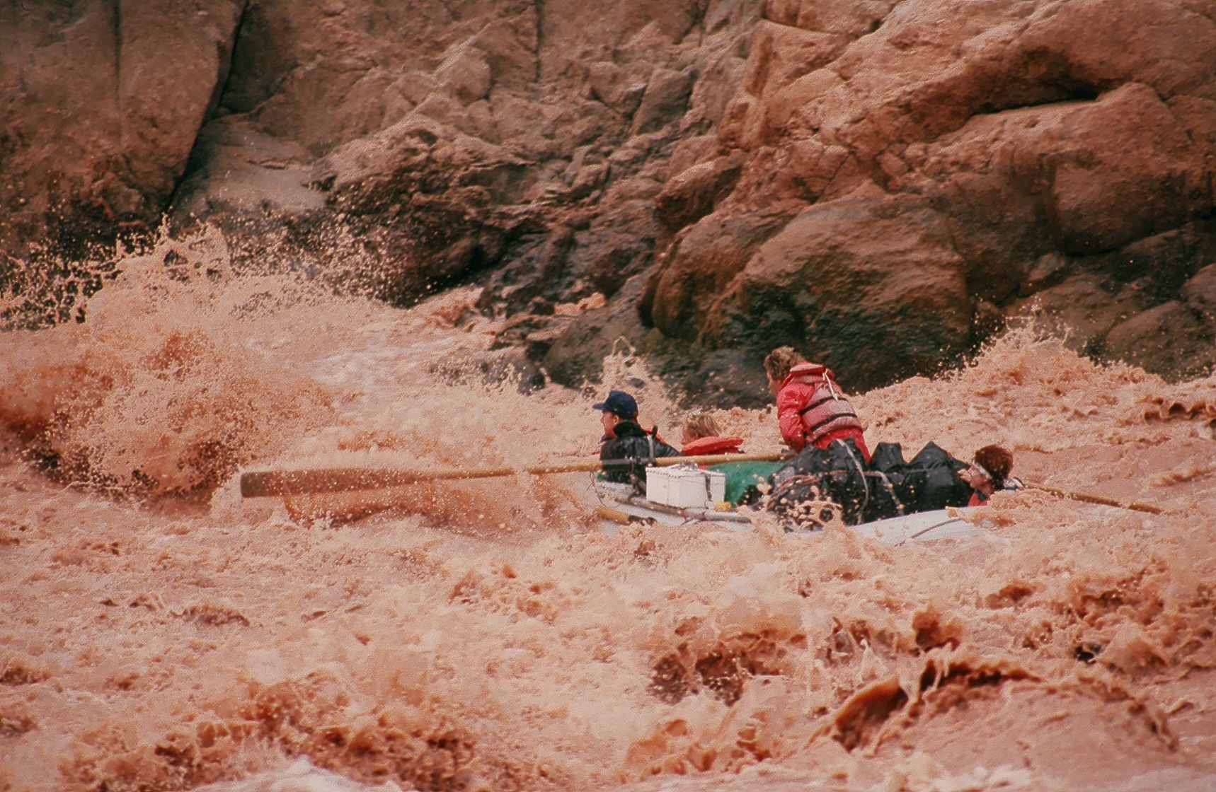 People on raft in turbulent, muddy water by brown rock formations