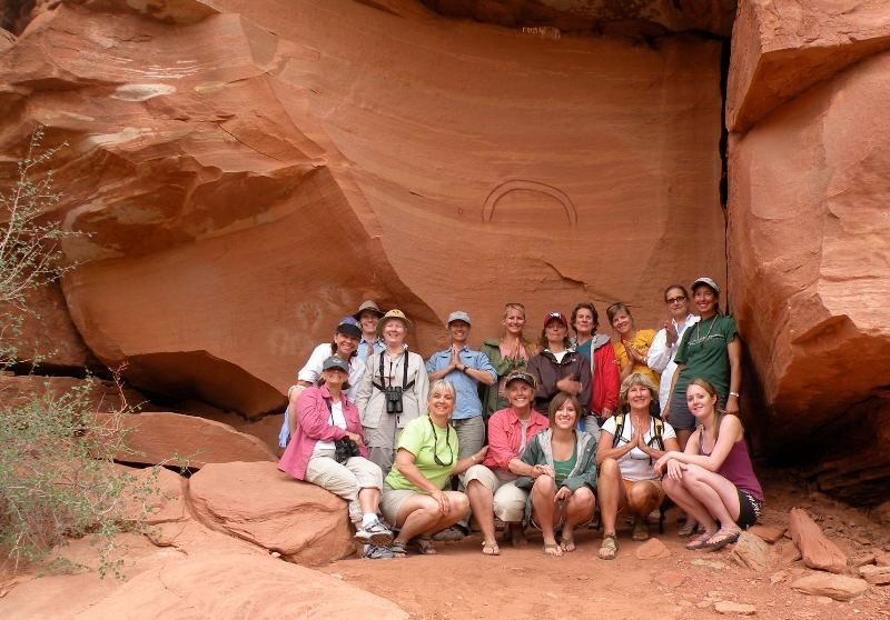 Group posing in front of a red rock formation with carved semicircular designs.