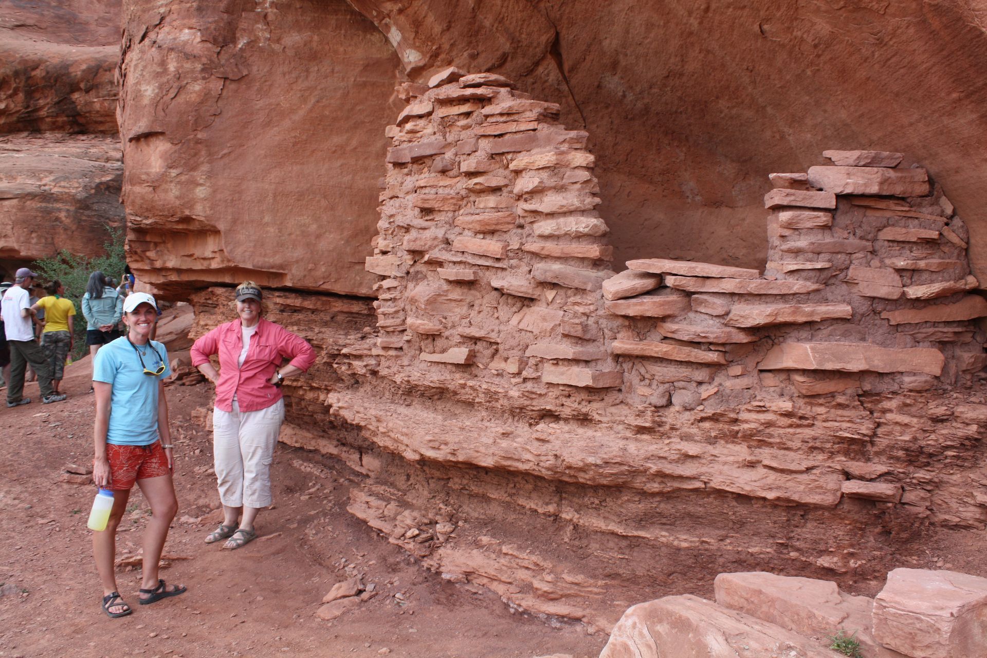People standing near a red rock structure with layered stonework.
