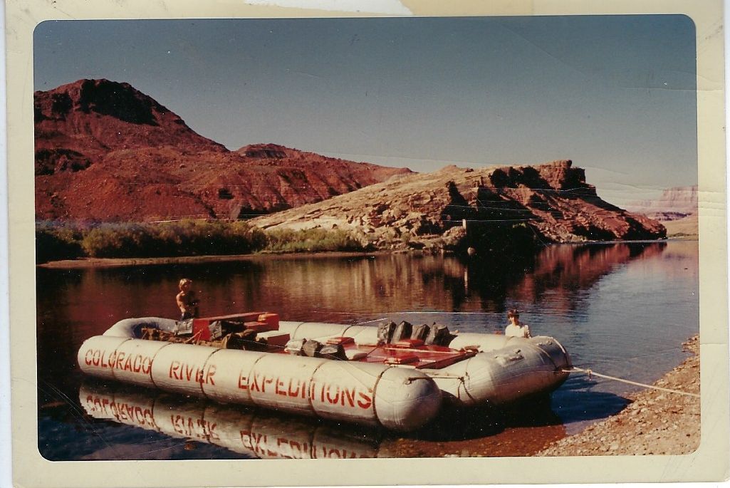 Rafting on calm river near red hills; raft is tied to shore, with the words 