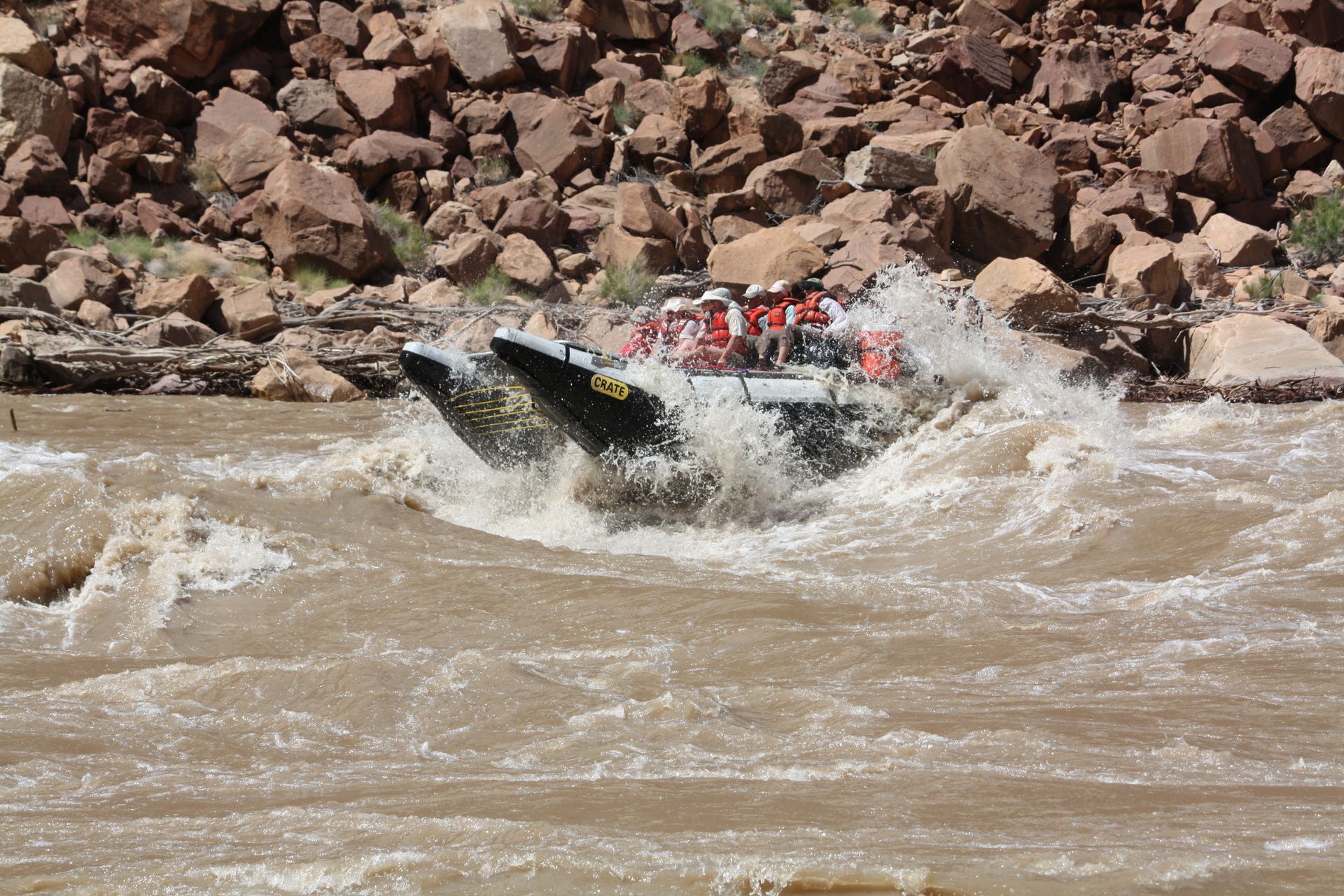 Whitewater rafting boat navigating rapids; splashing water, rocky background.