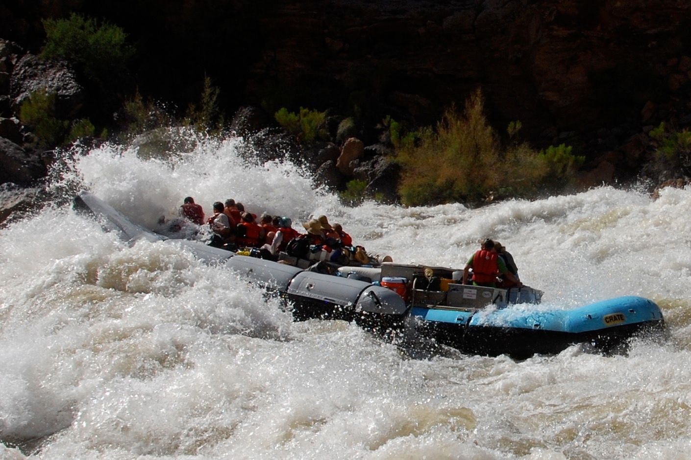 Rafting on whitewater rapids; raft filled with people, splashing through waves.