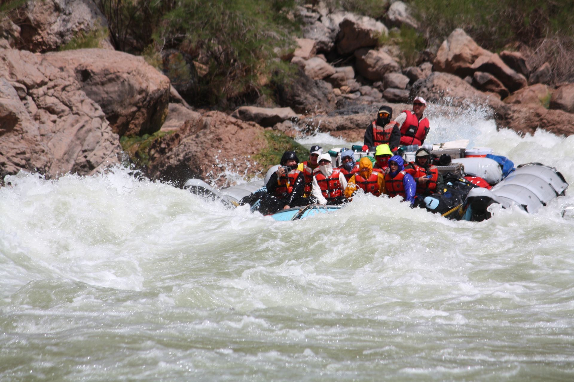 Rafting on whitewater rapids; passengers in life vests navigate turbulent, splashing water.