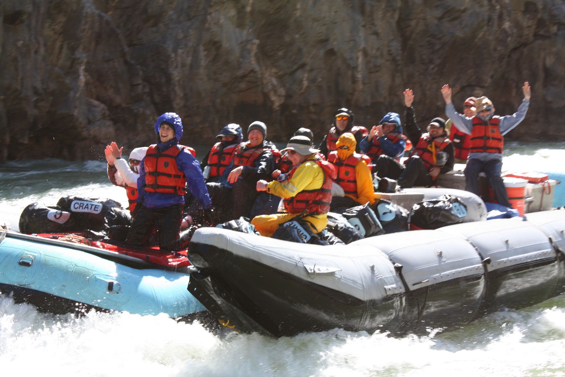 People in rafts navigating white water, arms raised in a canyon setting.