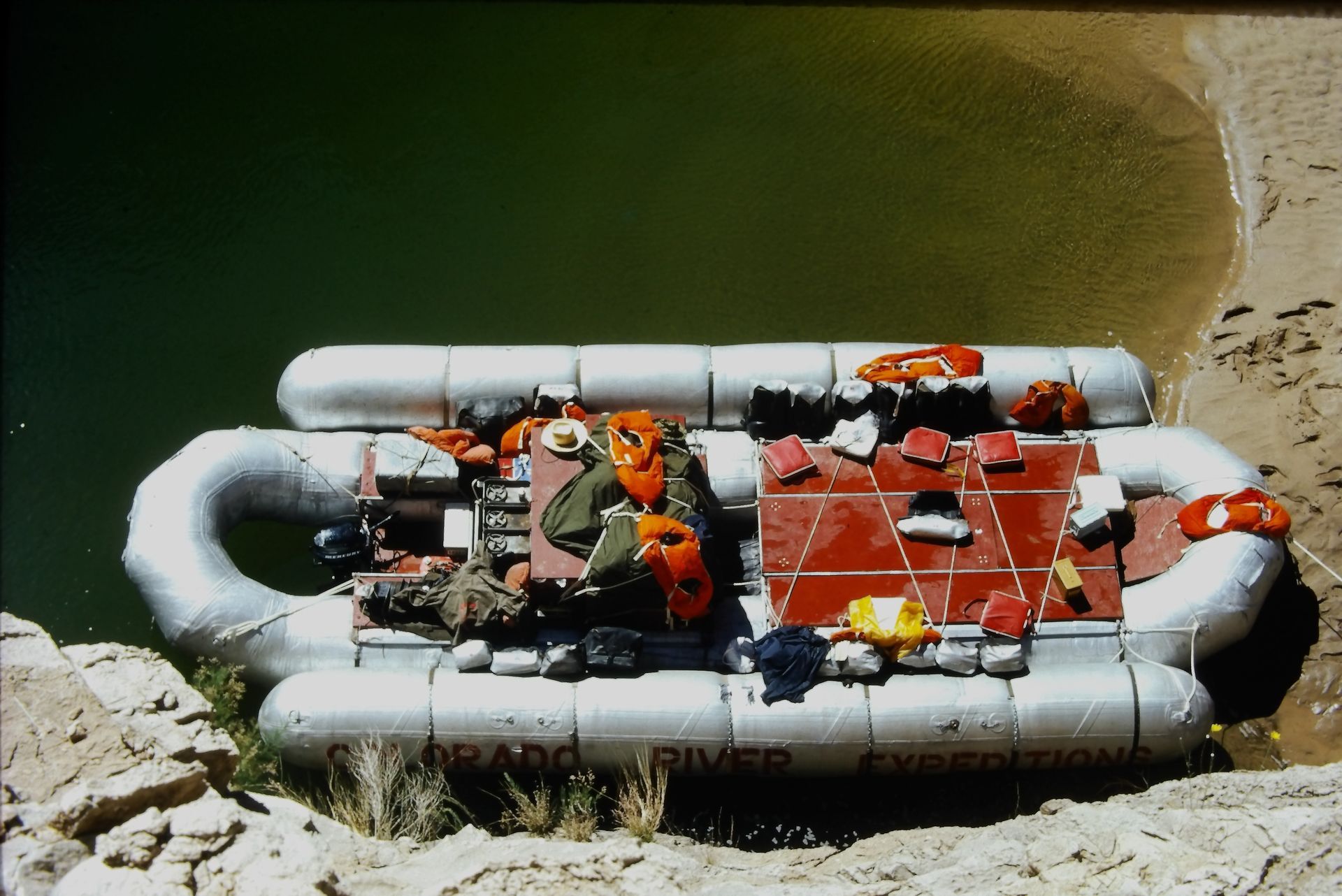Raft loaded with gear on the Colorado River. Beige and white raft, red, orange, and yellow gear.