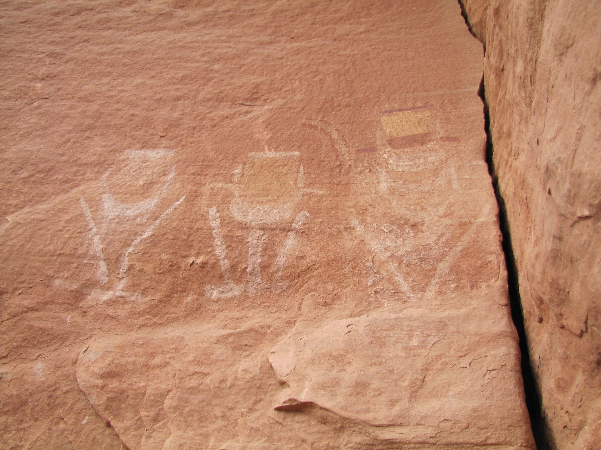 Rock art with three white figures outlined on red rock.