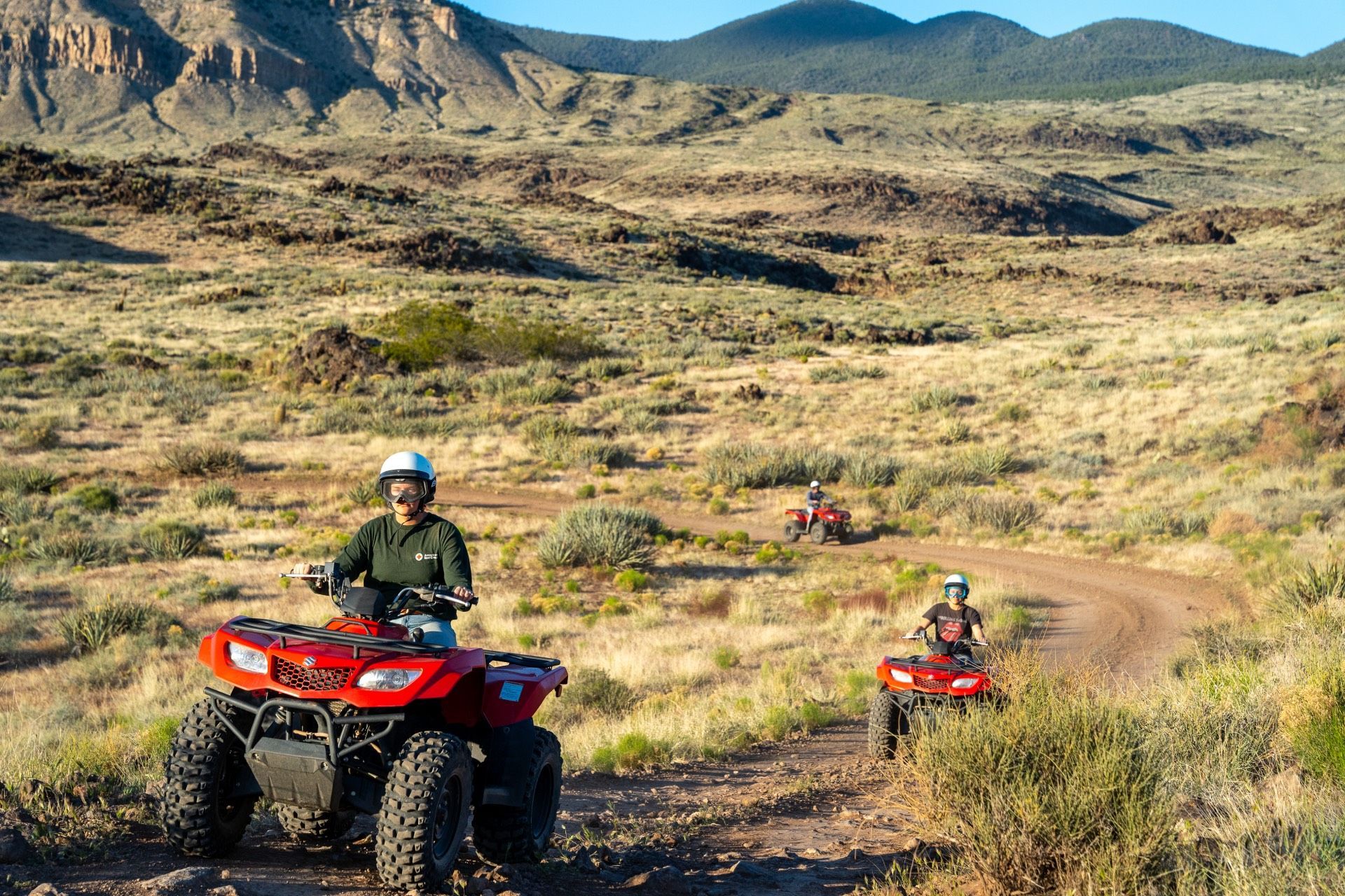 ATVs driving on a dirt trail in a desert landscape with mountains in the background.