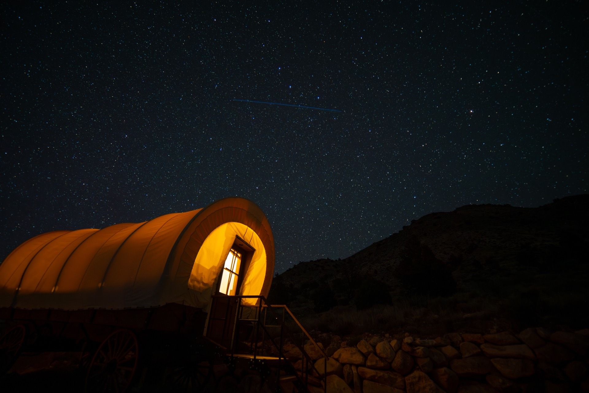 A lit covered wagon under a starry night sky.