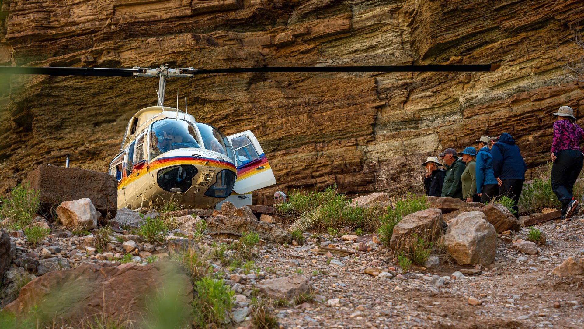 Helicopter crashed against a rock face. People walk towards the helicopter, possibly injured.
