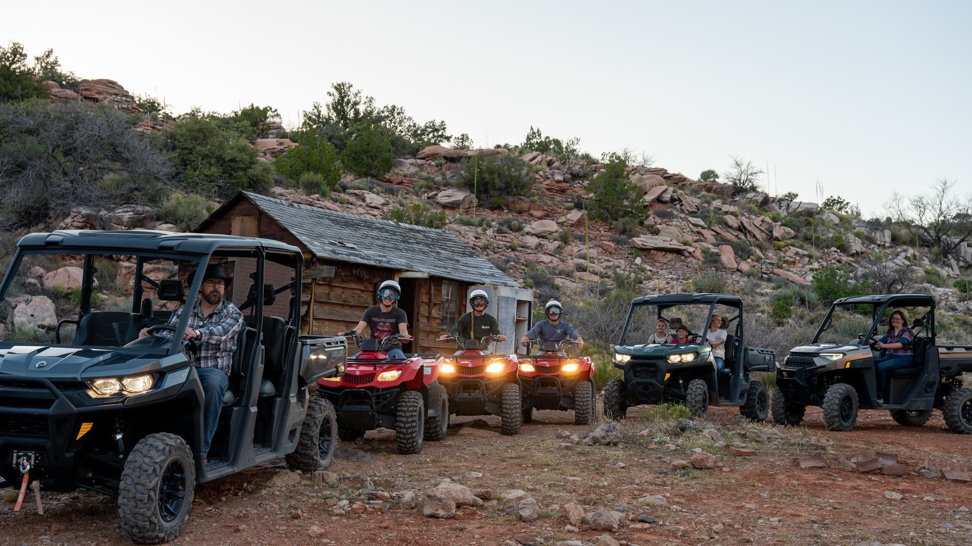 Group of people on ATVs in a rocky, outdoor setting near a small wooden building.