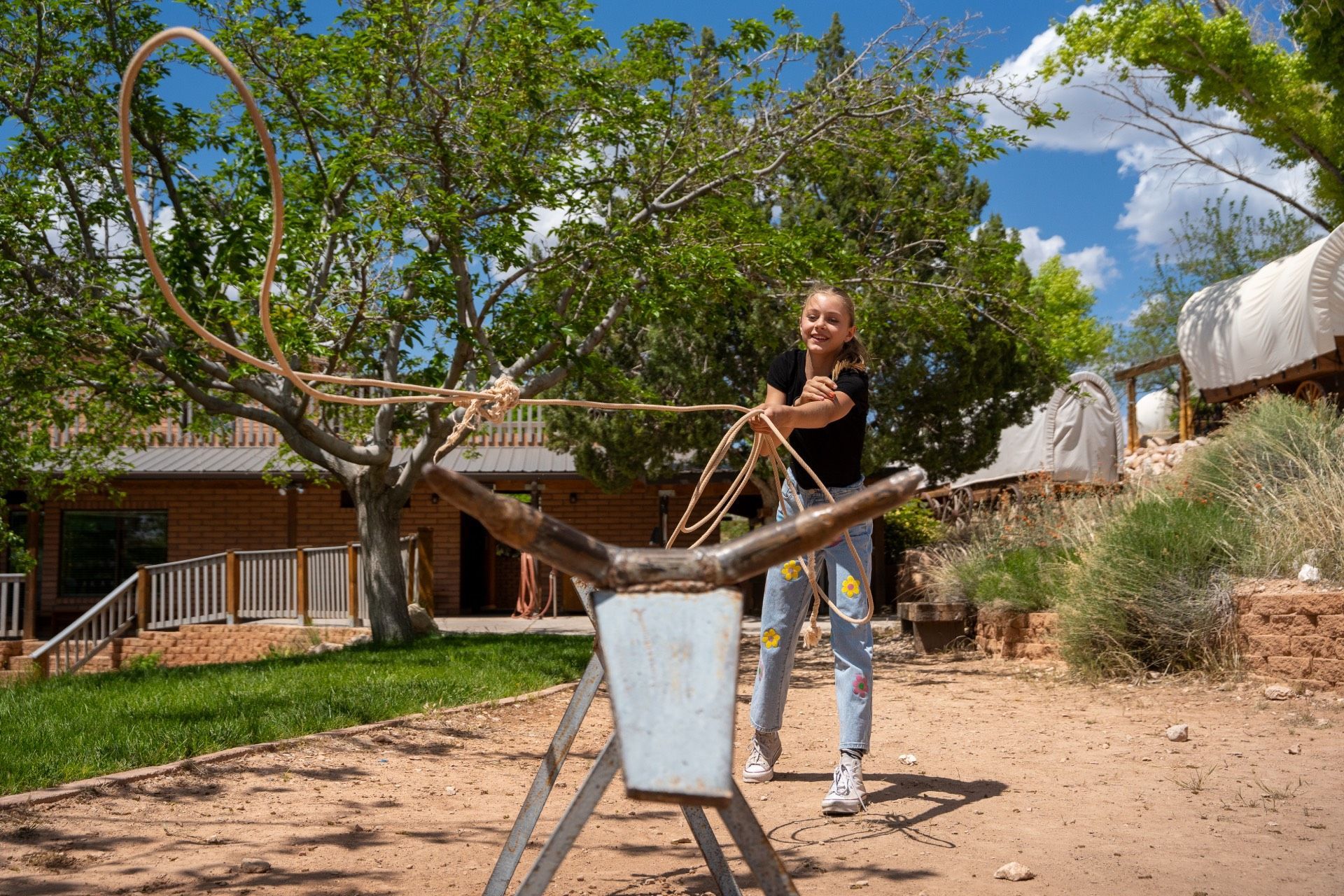 Girl practicing lasso with a rope loop on a bull head prop outdoors on a sunny day.
