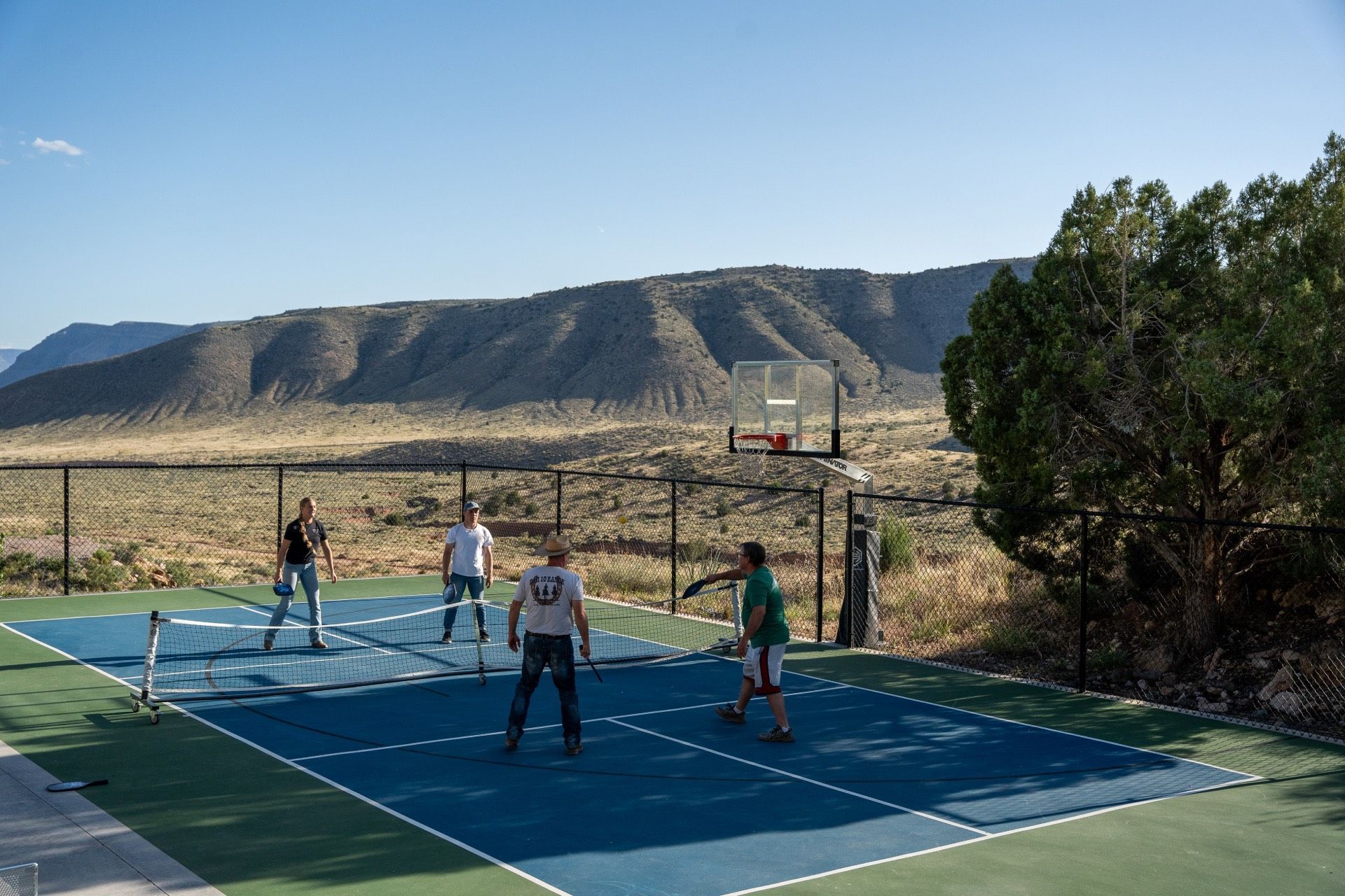 Four people playing pickleball outdoors with mountains in the background.