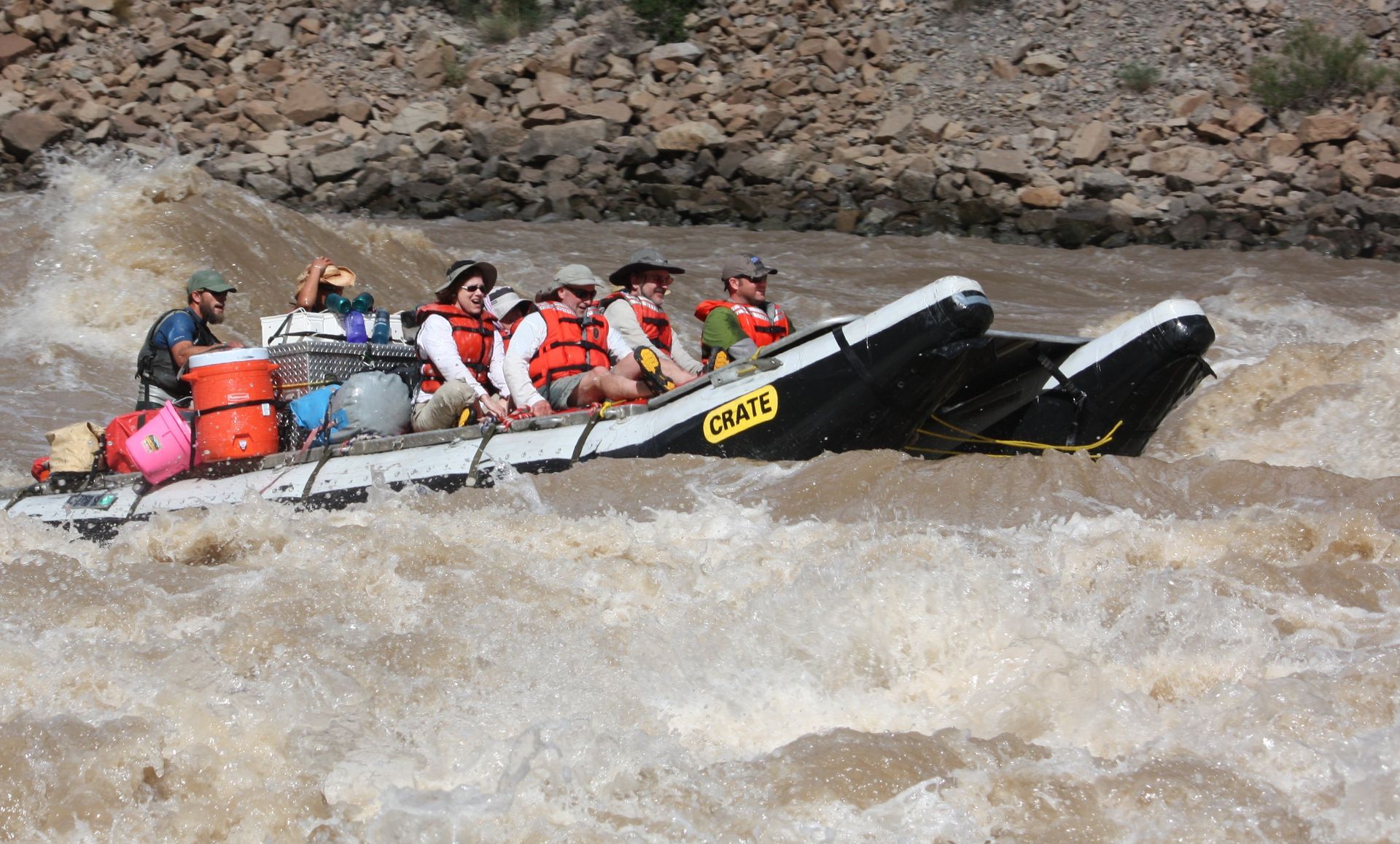Rafting on a brown river; several people in life vests navigate rapids.