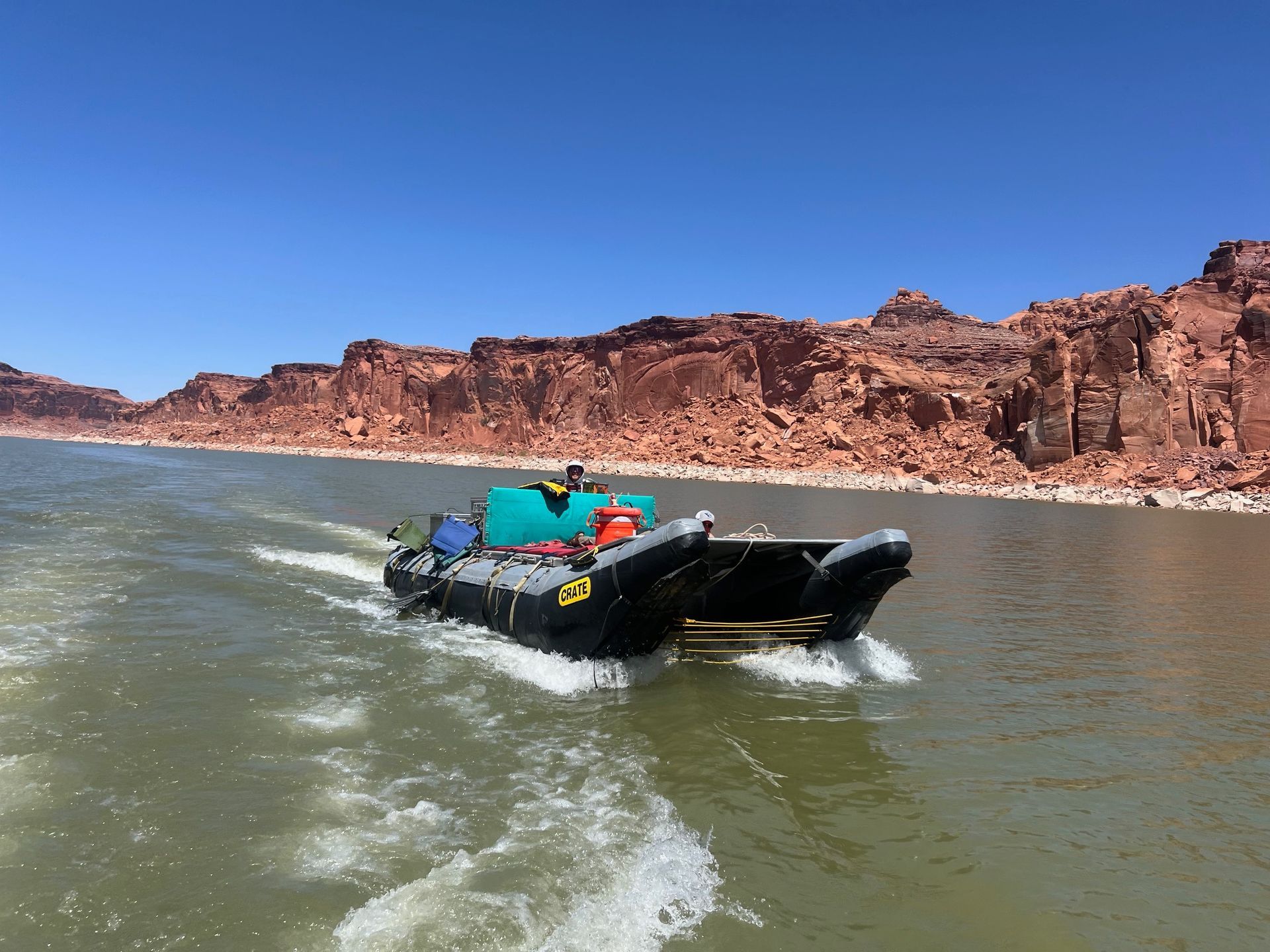 A black motorboat on water, with red rock cliffs in the background on a sunny day.