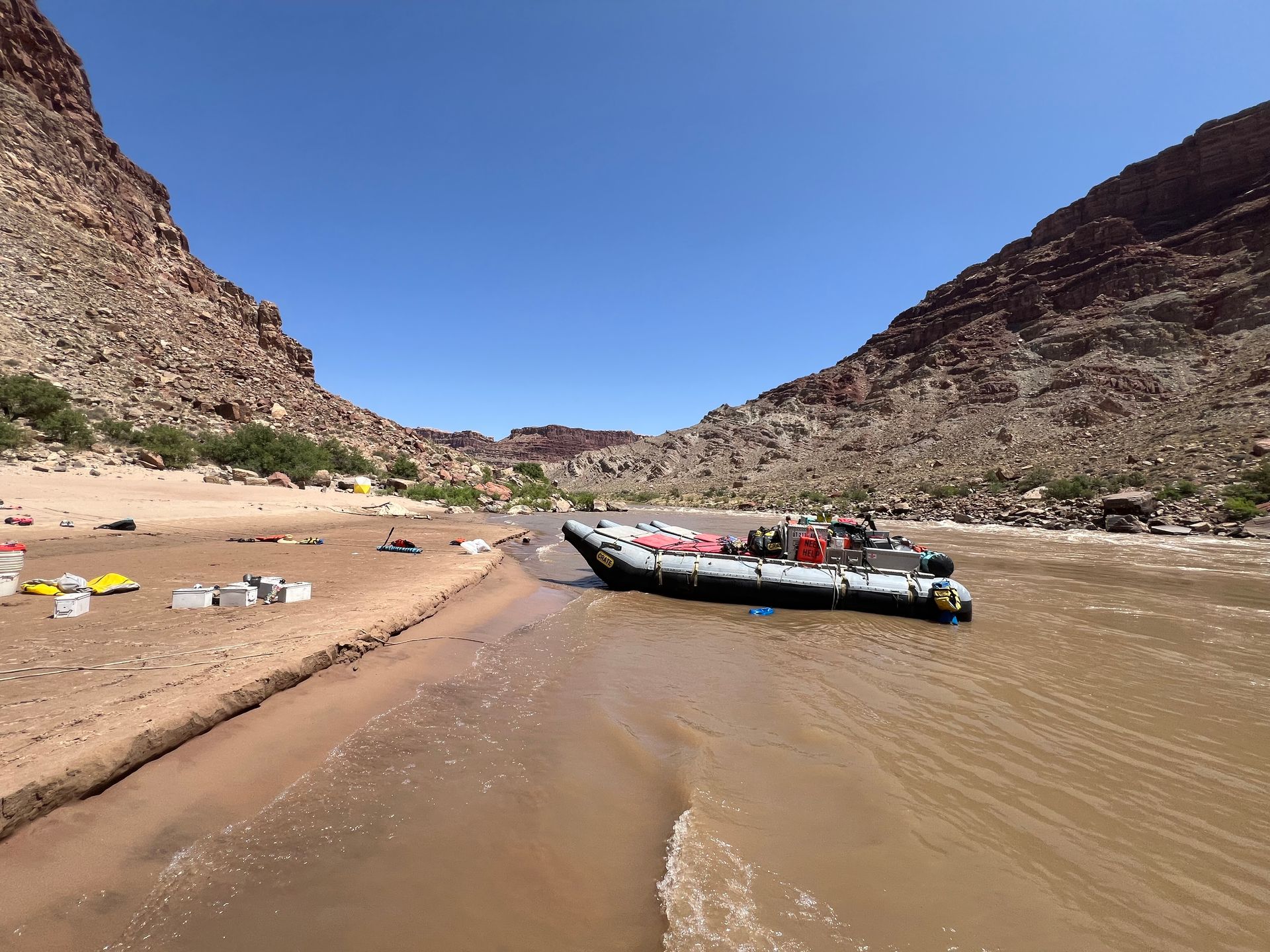 Raft on muddy riverbank, between canyon walls under blue sky.