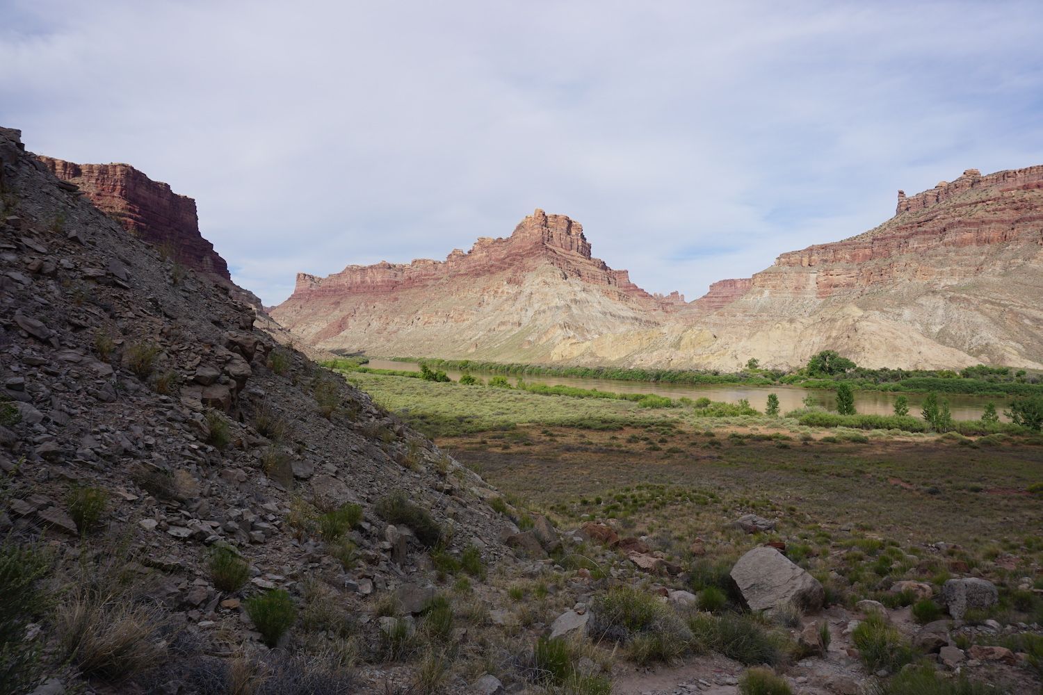 Rocky canyon landscape with red rock cliffs, green vegetation, and a cloudy sky.