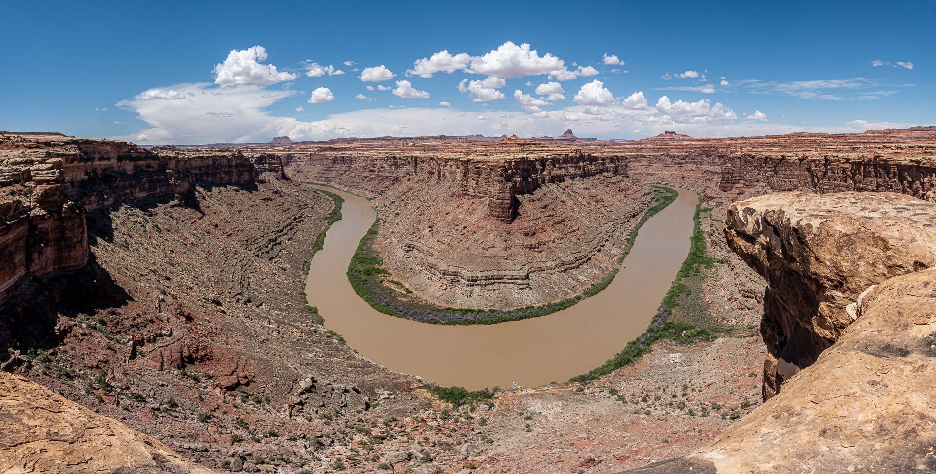 Brown river meanders through a red rock canyon under a blue sky with white clouds.