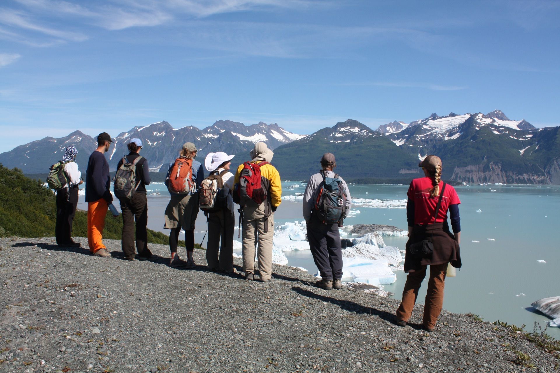 Group of people hiking, looking at glacier and mountains; sunny, blue sky.