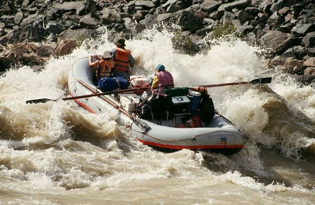 Rafting in white water. A gray and red raft navigates through rough rapids; spray surrounds.