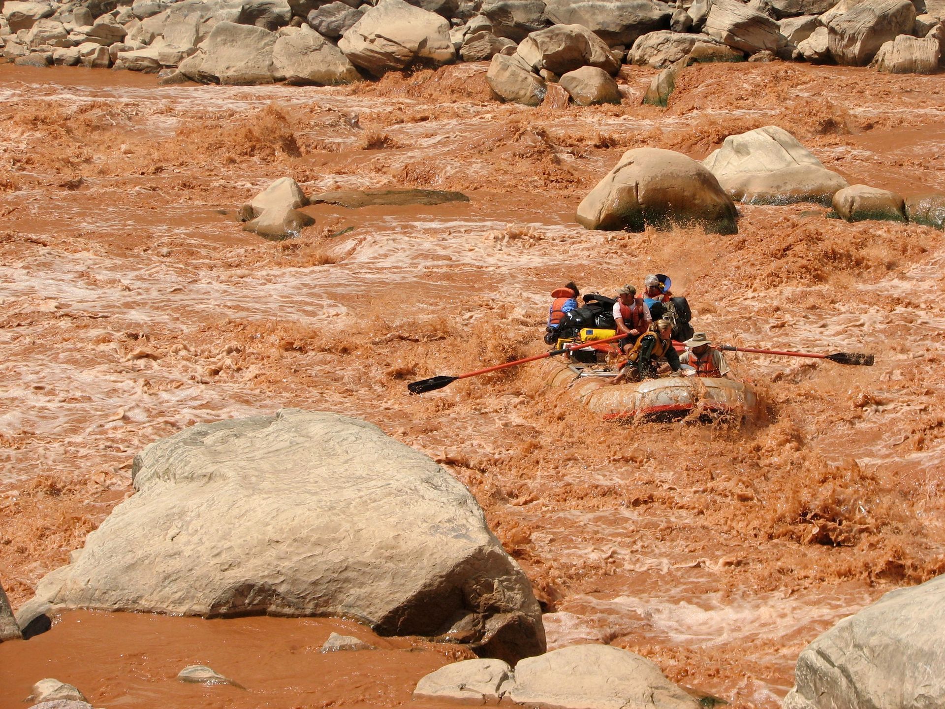 Rafting in a muddy, red river surrounded by large, light-colored rocks.